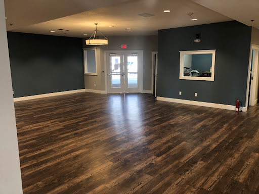 A spacious, modern interior room featuring wooden flooring and dark green walls, designed for versatility.