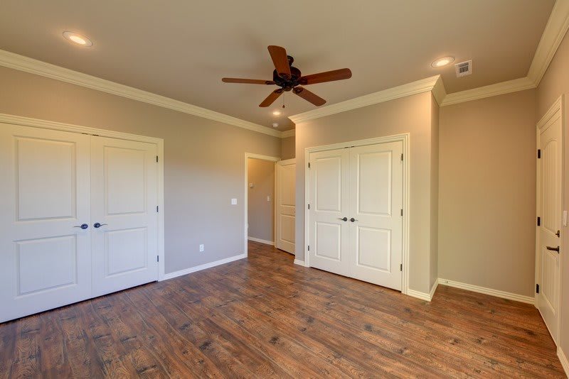 An empty room with wooden flooring, two doors, a ceiling fan, and crown molding.