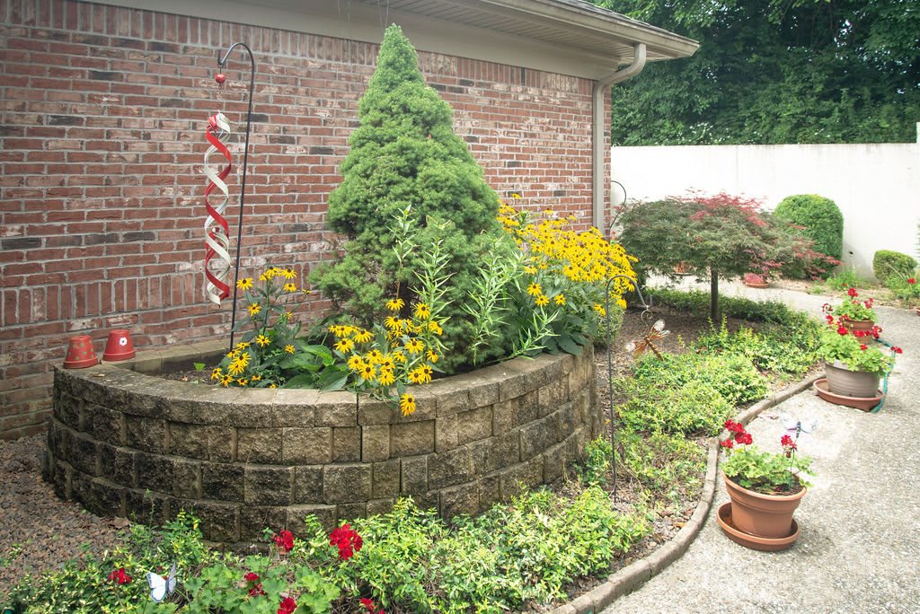 A beautifully landscaped garden with flowers and potted plants next to a brick wall.