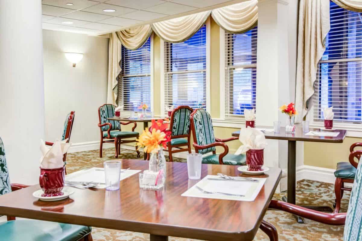 A cozy dining area with neatly arranged tables and chairs, decorated with floral centerpieces.