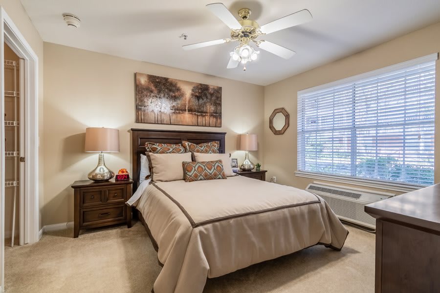 A cozy bedroom with neutral tones, featuring a neatly made bed, bedside tables with lamps, and a large window allowing natural light.