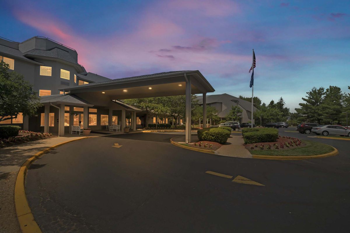 A hospital entrance at dusk with exterior lighting and a parking area.
