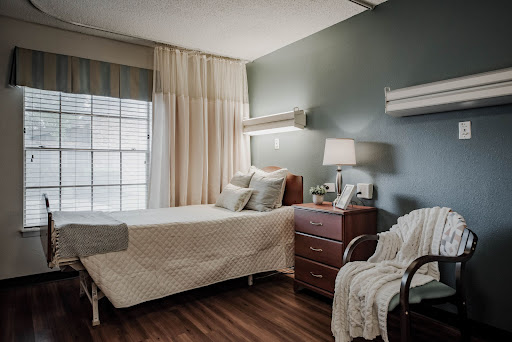 A serene hospital room featuring a neatly made bed, bedside table, and window with soft curtains.