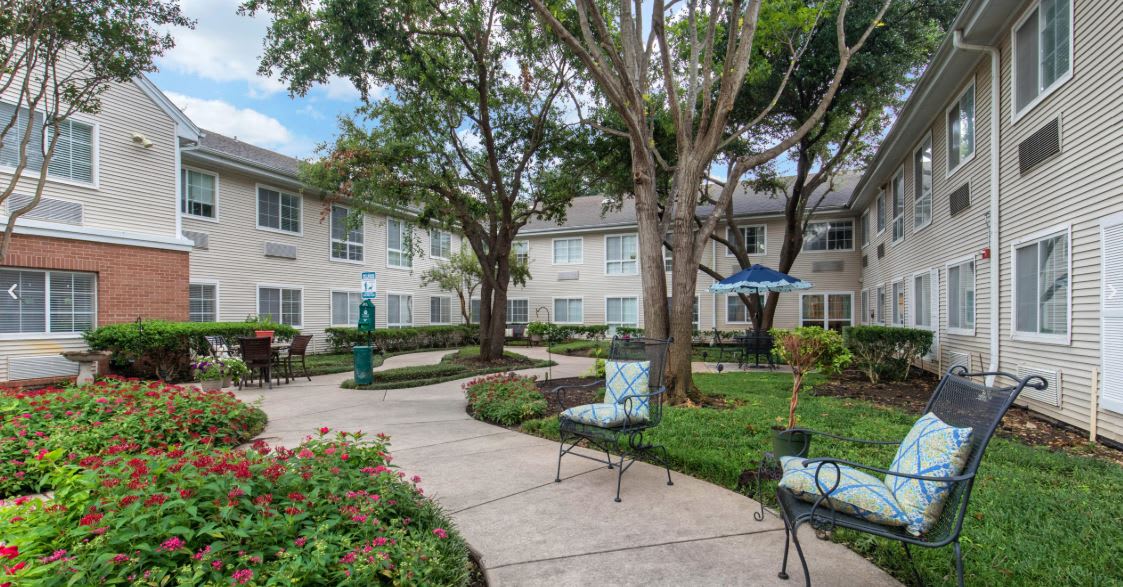 A well-maintained courtyard with benches and lush greenery in an apartment complex.