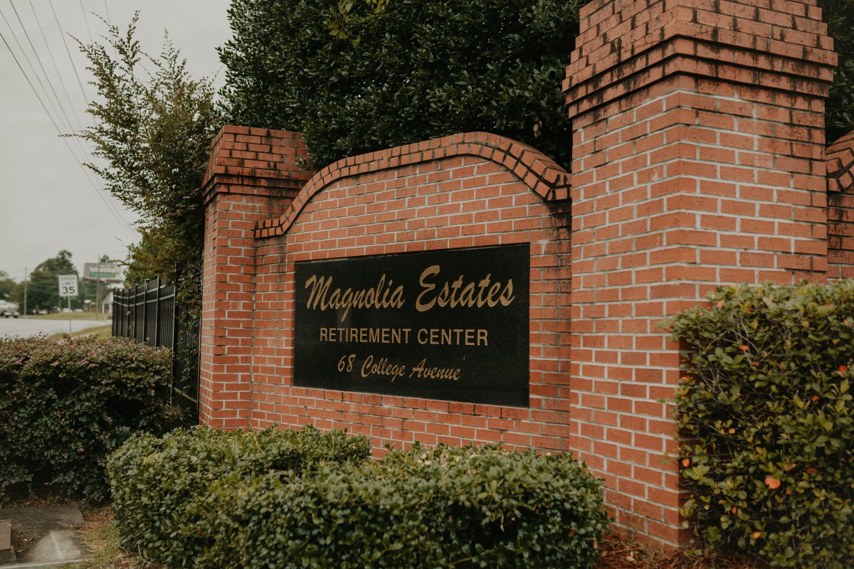 Entrance sign for Magnolia Estates Retirement Center, mounted on a brick wall surrounded by greenery.