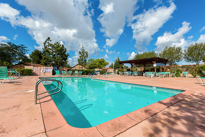 An outdoor swimming pool with surrounding chairs and tables under a partly cloudy sky.