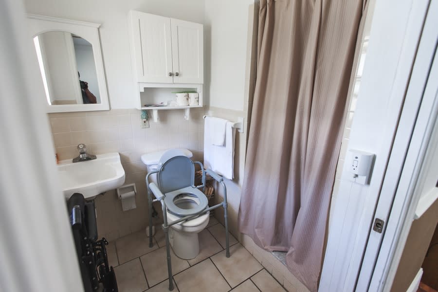 A small bathroom with a commode chair, sink, and shower curtain.