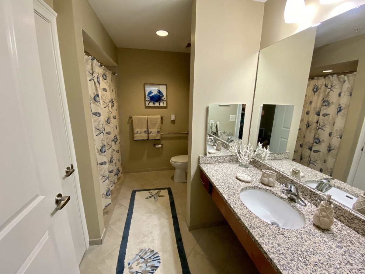 A clean and well-lit bathroom featuring a large mirror, granite countertop with a sink, towels, and a colorful shower curtain.