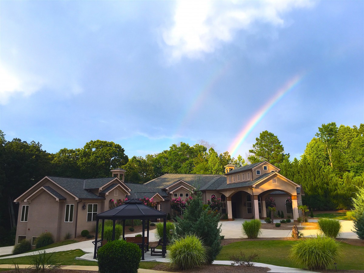 A beautiful mansion with a rainbow arching over it amidst a lush green backdrop.