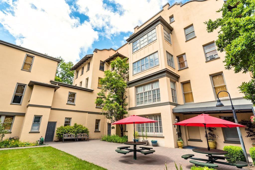 A courtyard with red umbrellas and outdoor seating beside a multi-story building.