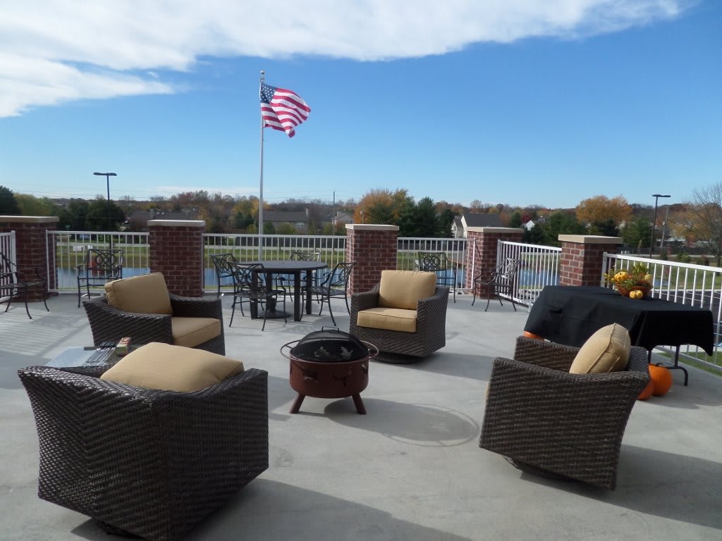 An outdoor patio featuring wicker chairs and a table, with an American flag waving in the background under a clear sky.