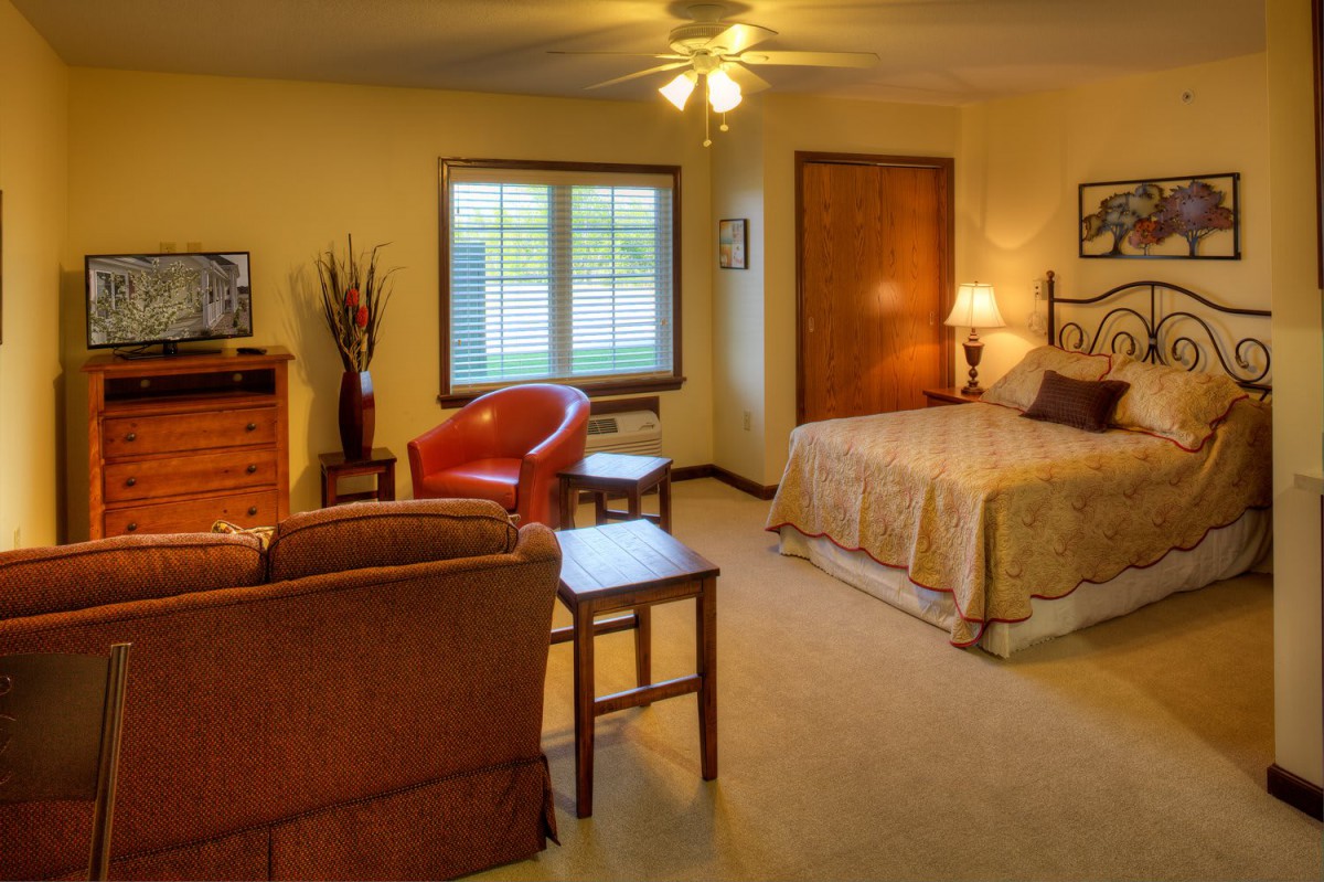 A cozy bedroom interior with a bed, seating area, and warm lighting.
