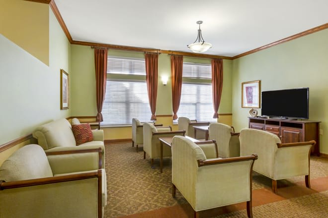 A cozy living room with several chairs and sofas arranged around a television, featuring elegant curtains and a carpeted floor.