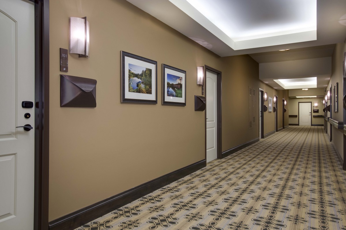 A hotel hallway with carpeted floors, wall-mounted lights, and framed artwork.
