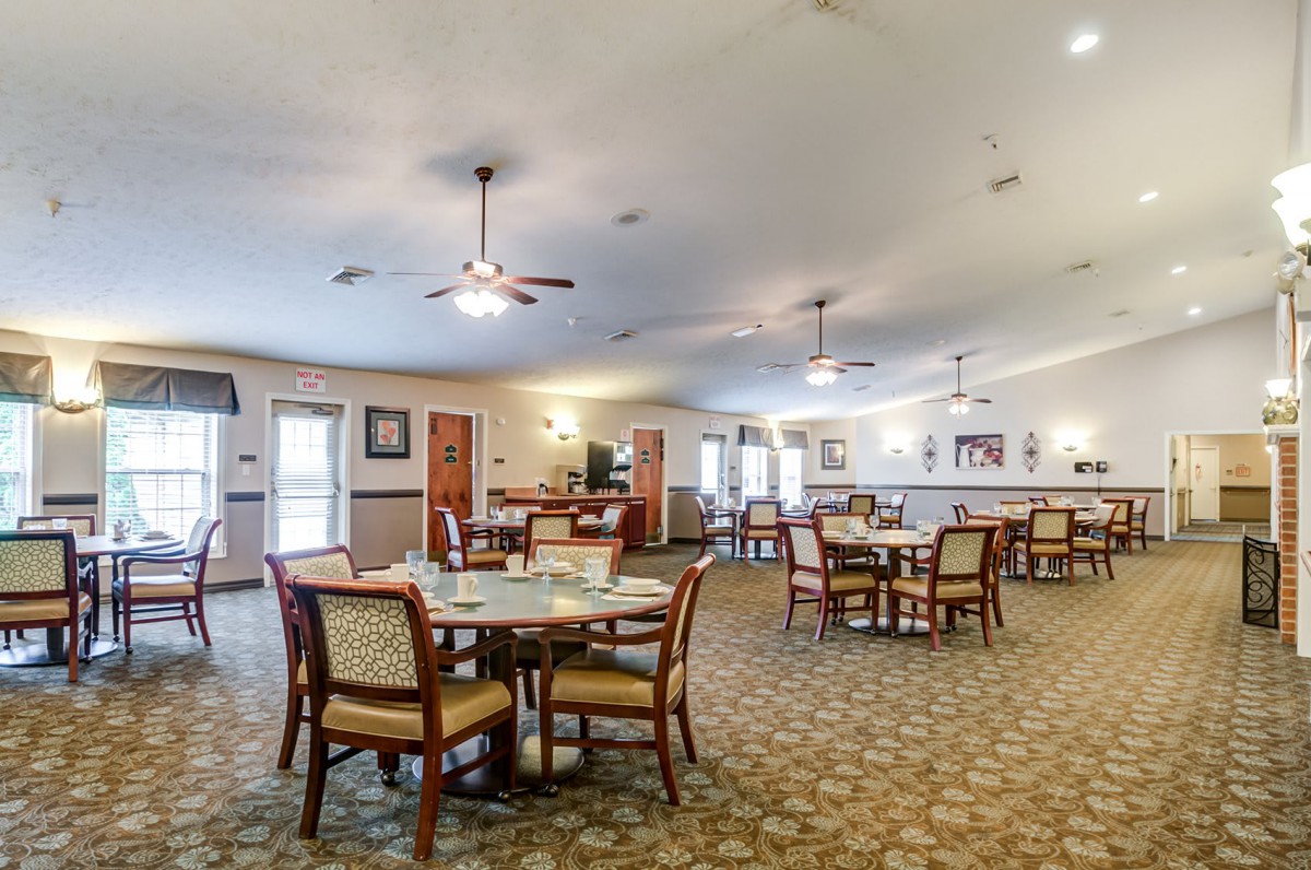 Spacious dining area with multiple tables and chairs, ceiling fans, and carpeted flooring.