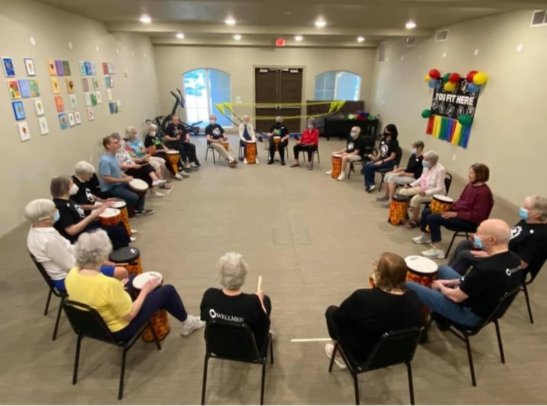 A group of people sitting in a circle participating in a drumming session indoors.