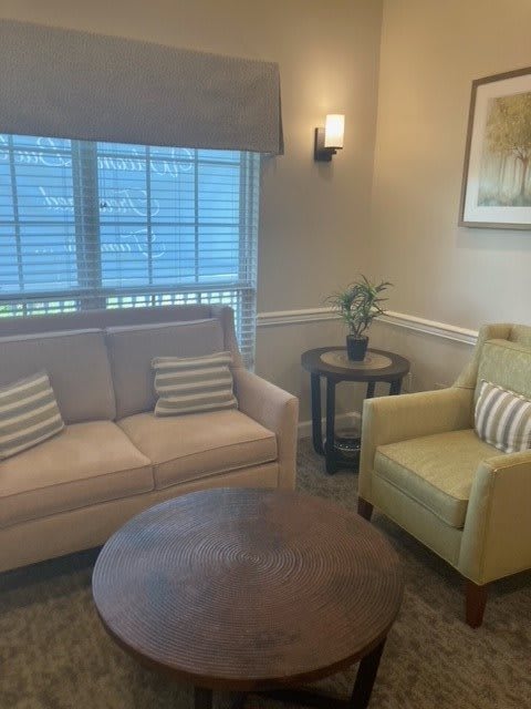 A cozy living room featuring a sofa, armchair, and coffee table near a window with blinds.