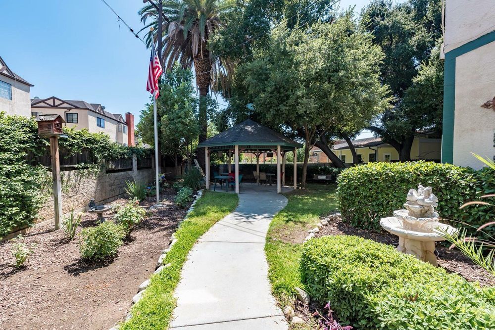 A pathway leads through a landscaped garden to a gazebo, surrounded by trees and shrubbery.