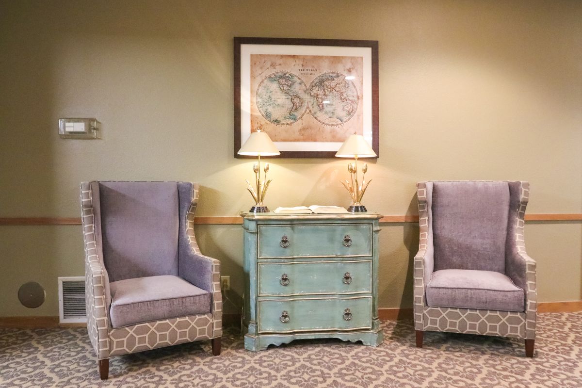 A cozy living room setup featuring two patterned chairs flanking a vintage blue cabinet, topped with elegant lamps and adorned with a framed world map.