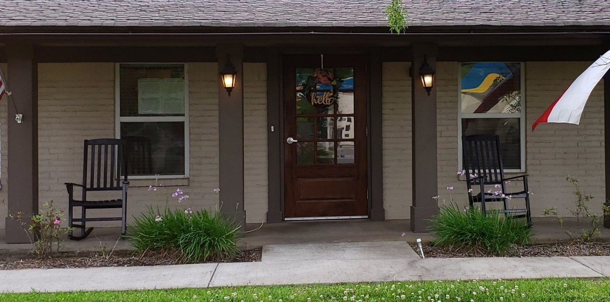 A welcoming front entrance of a house with a wooden door, porch lights, and landscaped greenery.