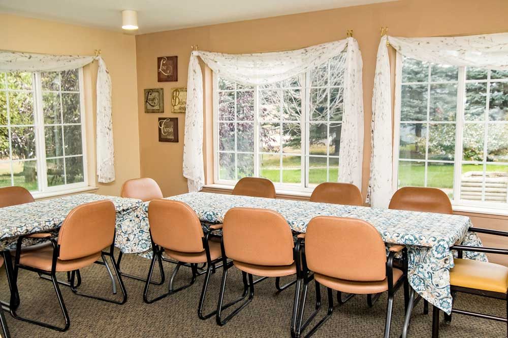 A meeting room with orange chairs around tables, featuring large windows with curtains.