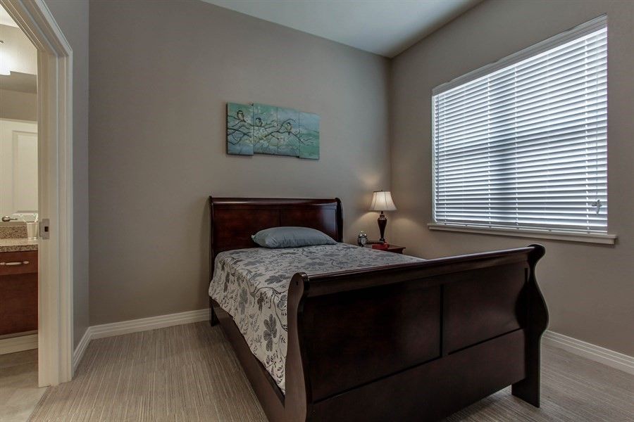 A cozy bedroom with a wooden bed, bedside lamp, and window with blinds.
