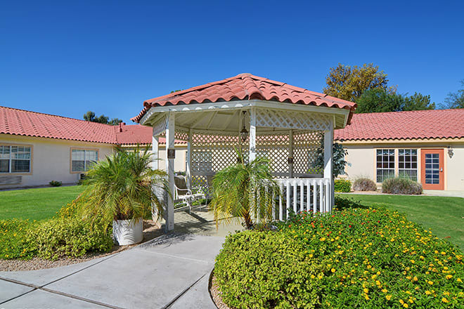 A charming gazebo set in a sunny garden with lush plants and a clear blue sky.