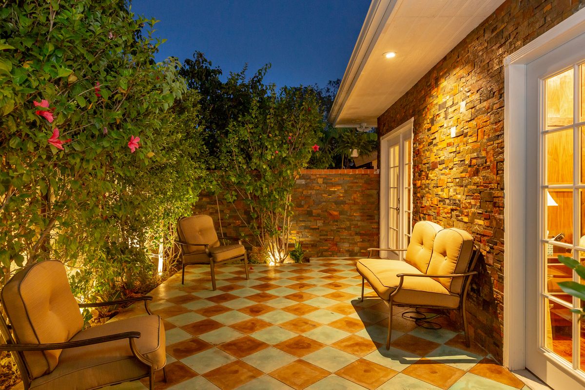 A cozy patio area illuminated at night with comfortable seating, surrounded by potted plants and a brick wall.