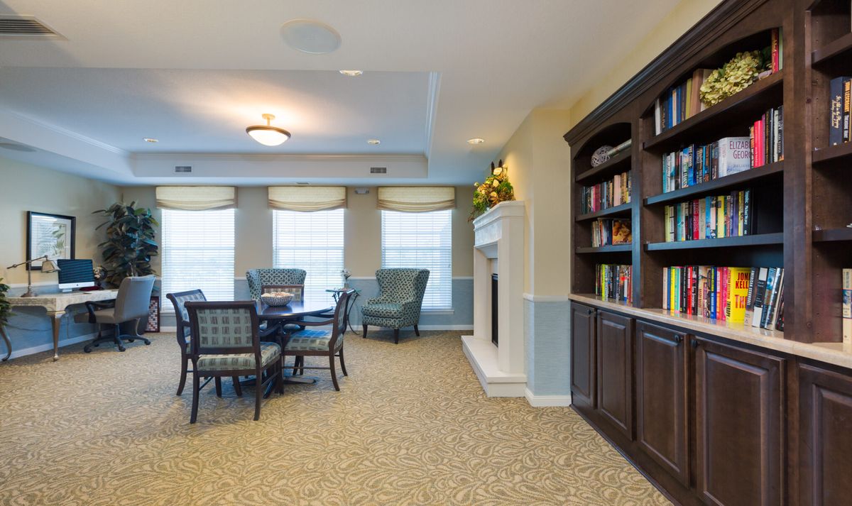 A cozy living room with a library, featuring bookshelves, a fireplace, and a seating area with a table and chairs.