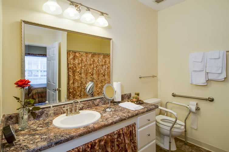 A bathroom with a granite countertop, sink, mirror, and toilet.