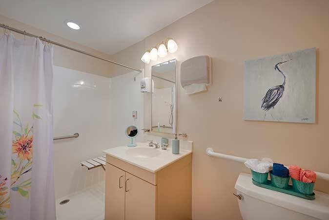 A modern bathroom featuring a sink, mirror, and toilet, with a walk-in shower and bright lighting.