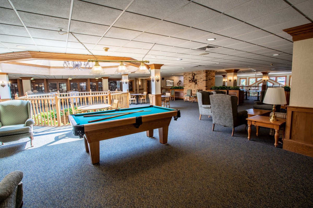 A lounge area with a pool table and comfortable seating, well-lit by indoor lighting.