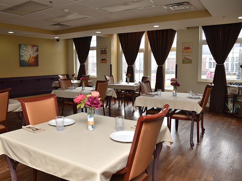 An elegant dining room with neatly arranged tables and chairs, featuring dark curtains and wooden flooring.