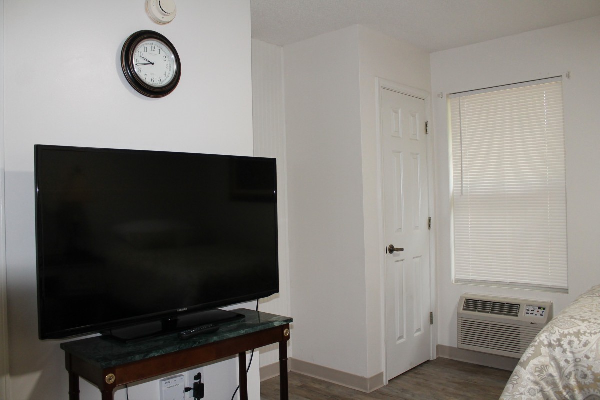 A minimalist living room featuring a television, a clock on the wall, and a door.