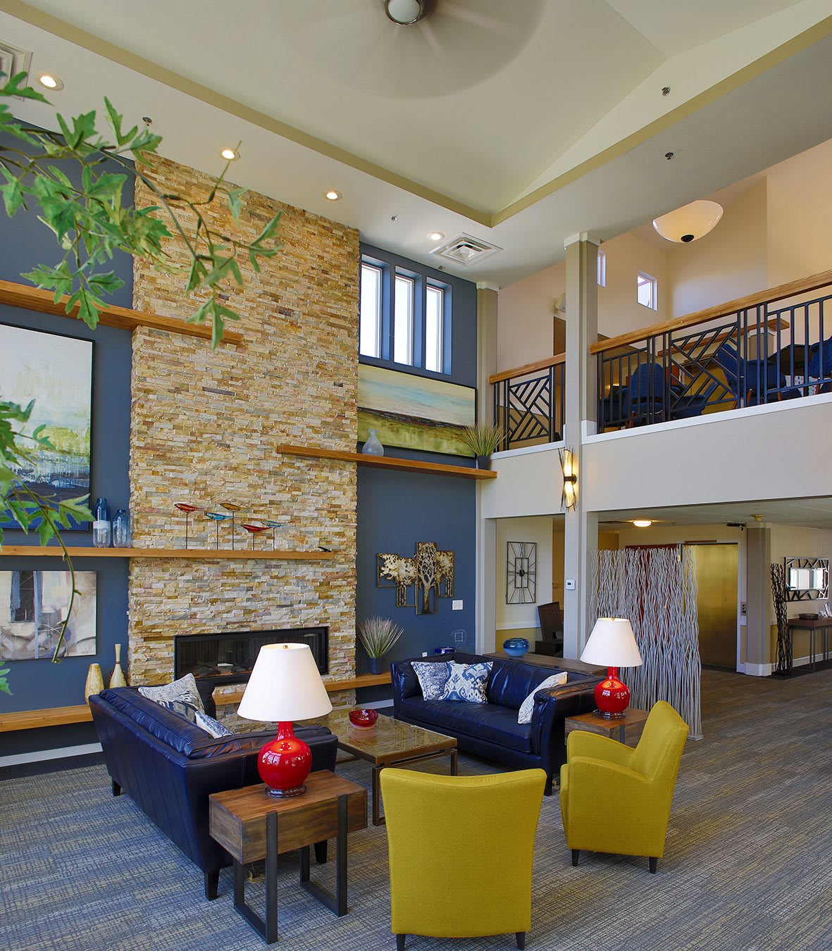 A spacious and modern living room with a stone fireplace, colorful decor, and loft area.