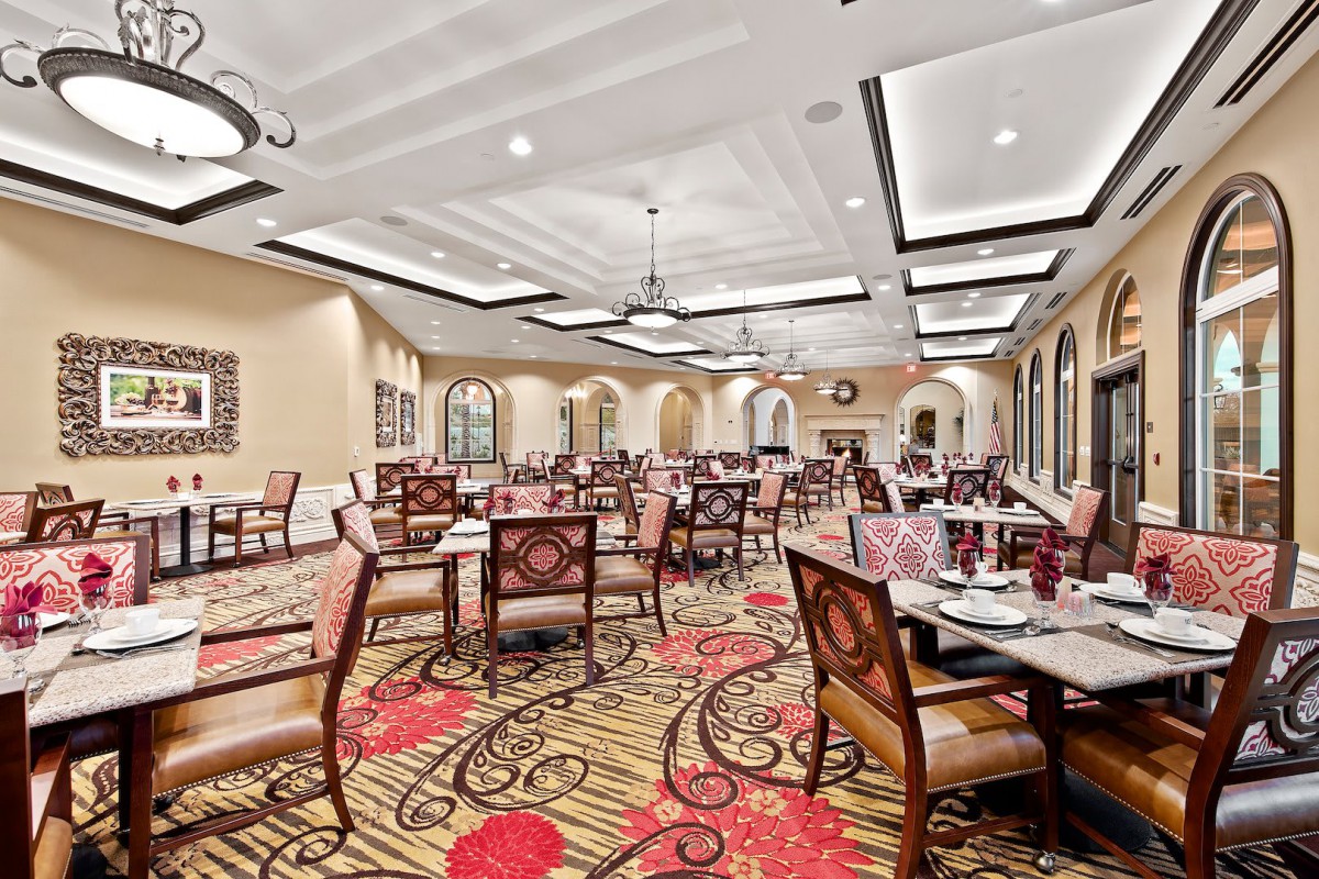 An elegant restaurant dining room with beautifully arranged tables and chairs, featuring a decorative carpet and stylish lighting.