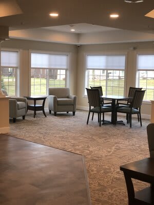 A cozy living room with chairs and a table near large windows letting in daylight.