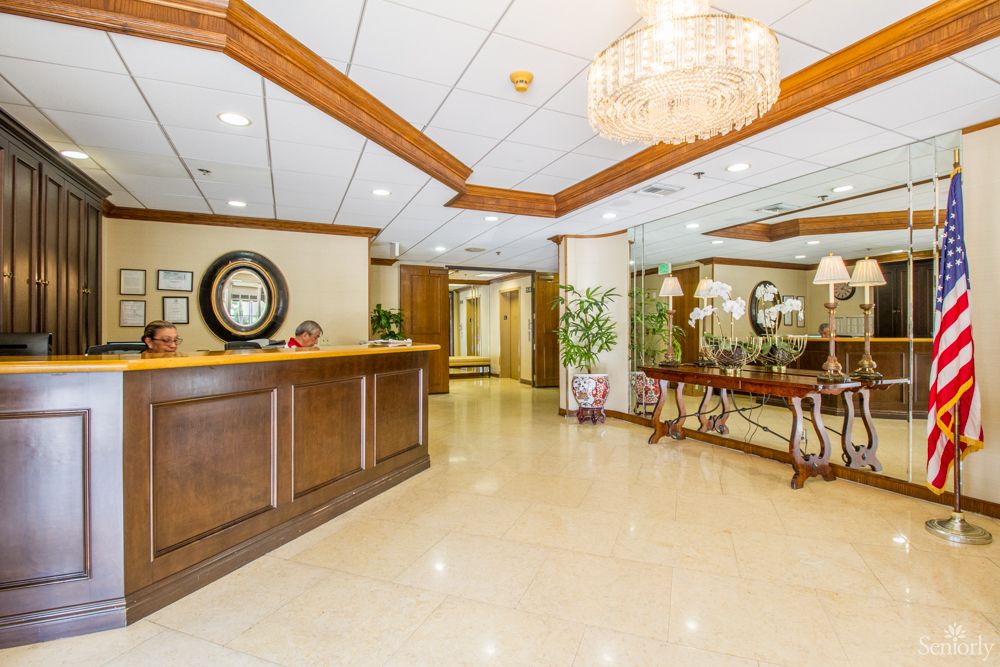 A spacious lobby area with a wooden reception desk, decorative mirrors, and elegant lighting.