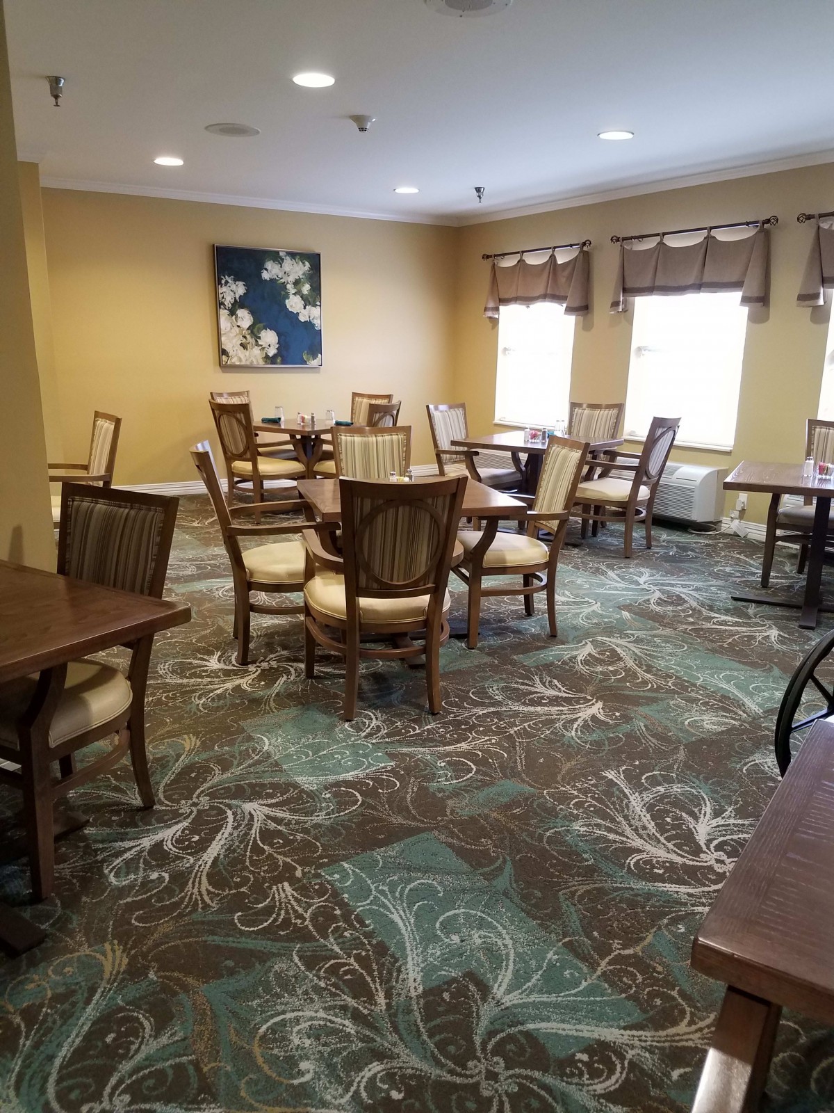 A well-lit dining room with multiple tables and chairs arranged on a patterned carpet.