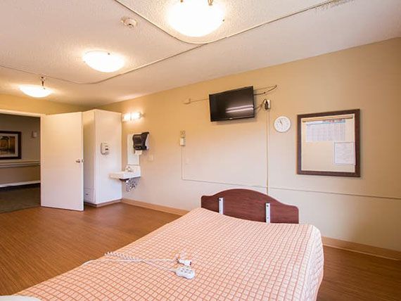 A clean, well-lit hospital room with a single bed and a wall-mounted television.