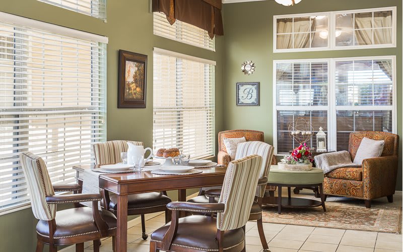 A cozy dining area with a wooden table, upholstered chairs, and abundant natural light streaming through multiple windows.