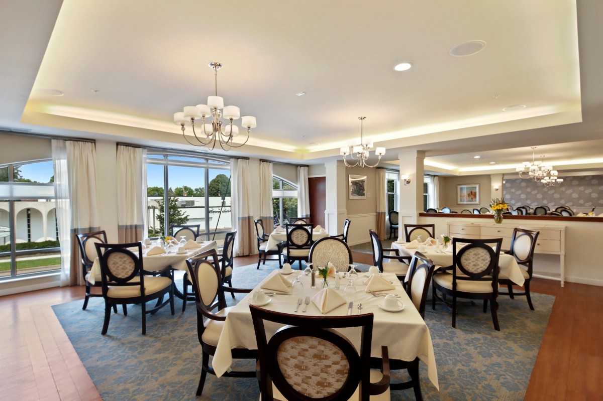 An elegant dining room with neatly arranged tables and chairs, adorned with chandeliers and large windows providing ample natural light.