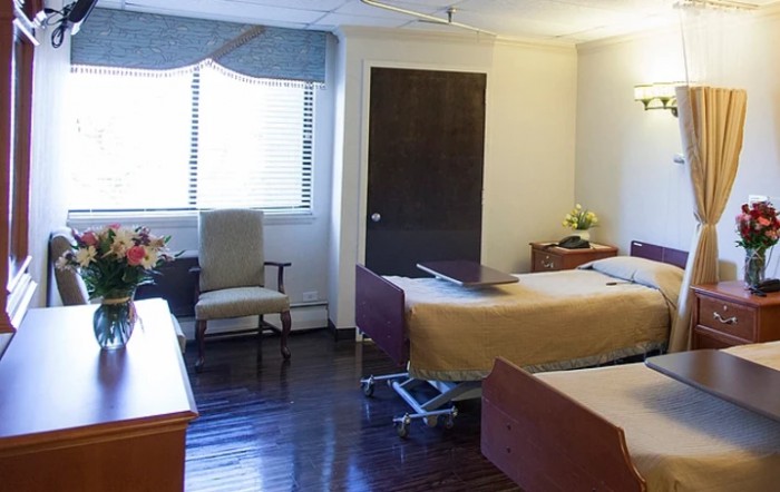 A hospital room with two patient beds and wooden flooring.