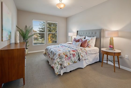 A cozy bedroom with a large bed, bedside tables, and natural light from windows.