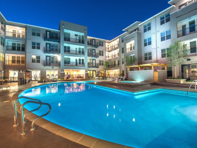 A modern apartment complex with a brightly lit swimming pool at night.