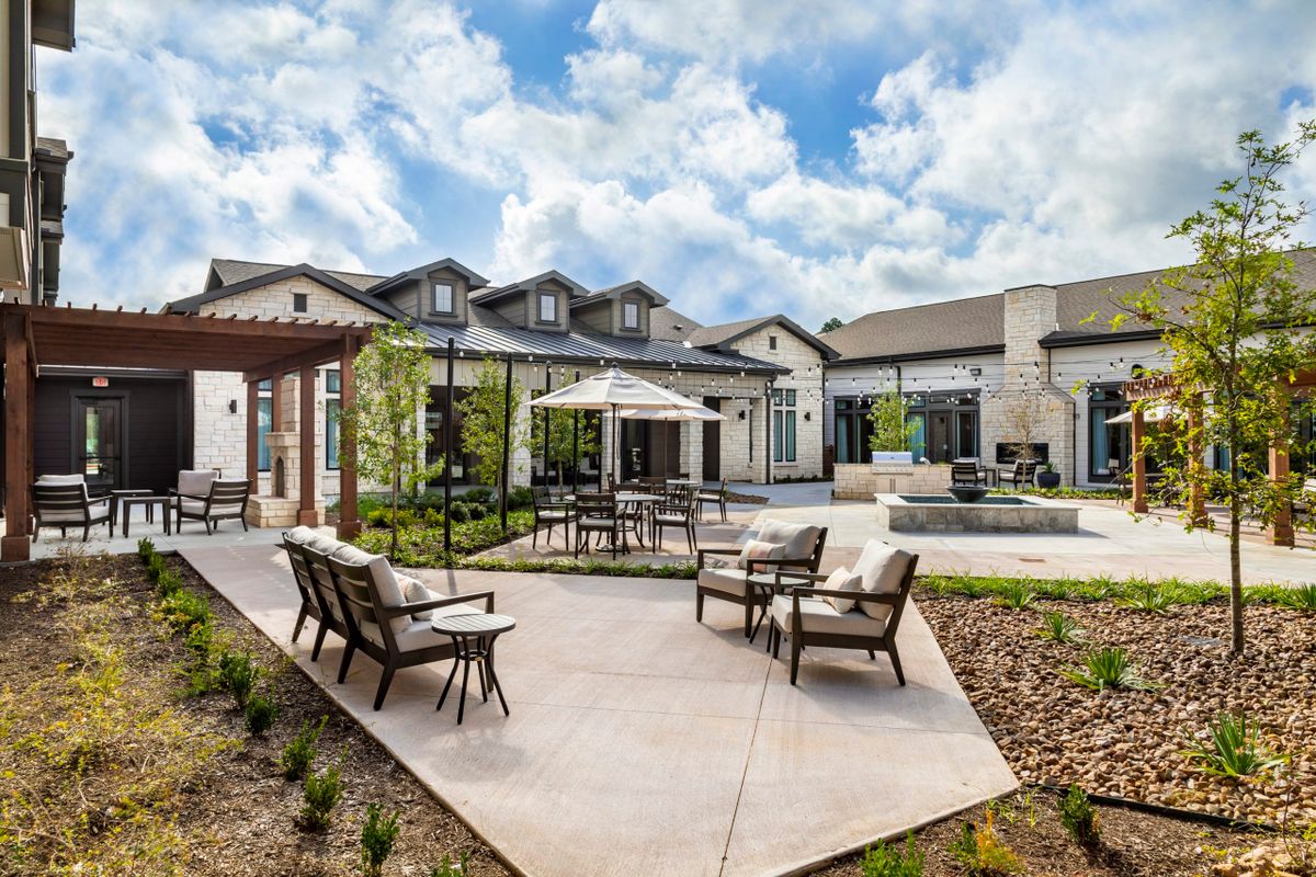 A spacious modern outdoor patio area with comfortable seating and a table under an umbrella, surrounded by landscaped gardens.