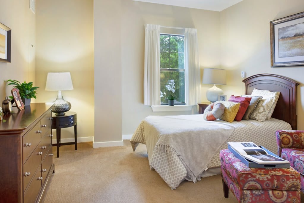 A cozy bedroom features a bed with decorative pillows, lamps on nightstands, and a window letting in natural light.