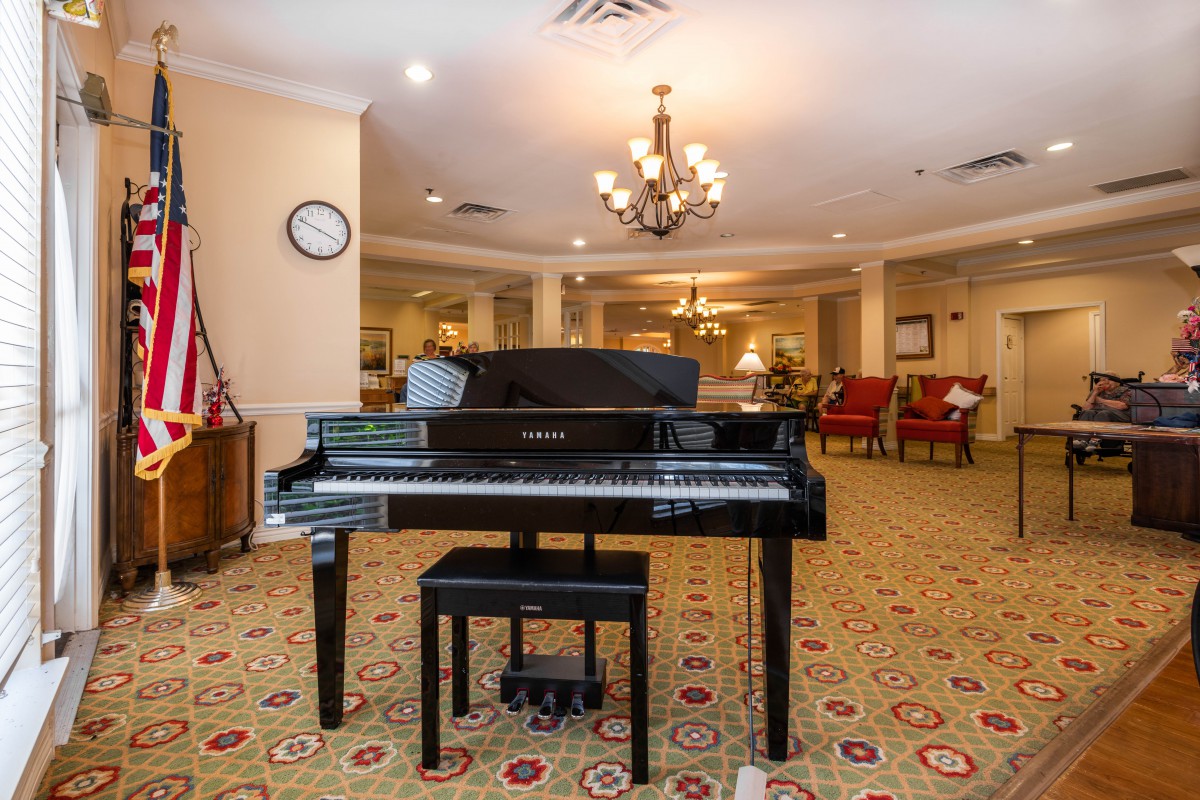 A grand piano in a warmly decorated living room with a chandelier.