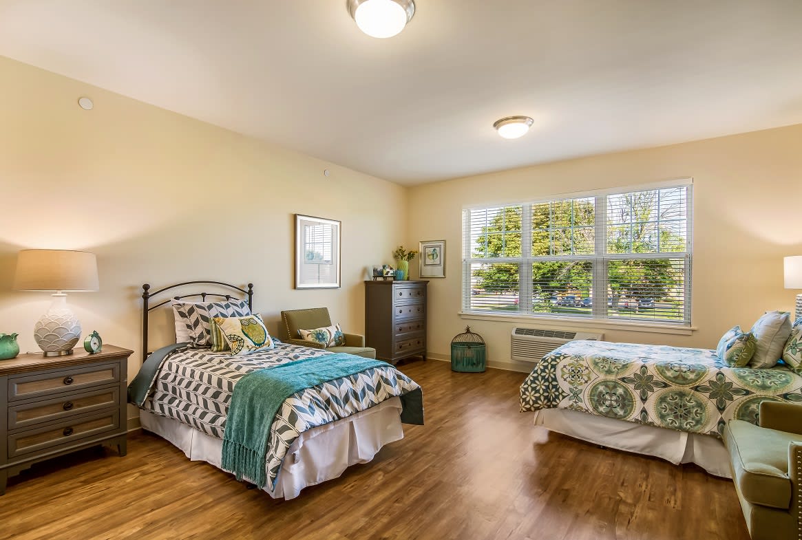 A cozy bedroom with two beds, stylish decor, and a large window overlooking greenery.