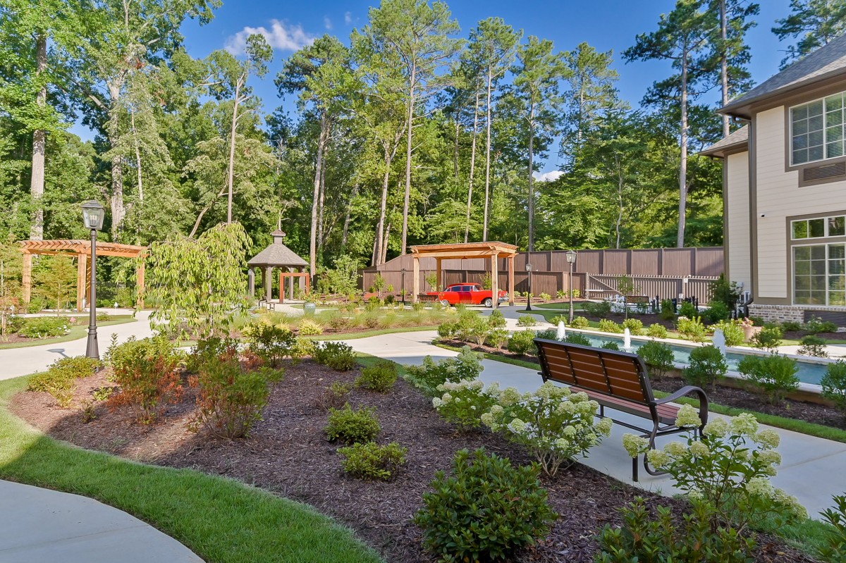A beautifully landscaped garden with a pathway, benches, and a gazebo surrounded by lush greenery.